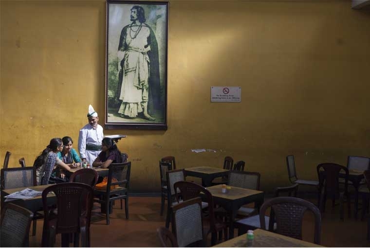 The Palaces of Memory ©Stuart Freedman, A waiter serves schoolgirls beneath a portrait of Rabindranath Tagore in the Indian Coffee House, Kolkata, 2013, C-type print Courtesy Tasveer